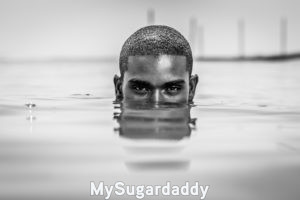 Se puede ver a un hombre sumergido en el agua hasta los ojos. Tiene una mirada seductora y profunda. La imagen esta en blanco y negro. Pelo corto y cejas negras. Parece tener una fuerte personalidad para coquetear. 