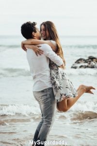 Relación nueva: sentimientos increibles Relación nueva: En esta imagen vemos a la chica tirarse en los brazos del hombre. Se ven muy felices y se miran directamente a los ojos. Están disfrutando de un día de playa.