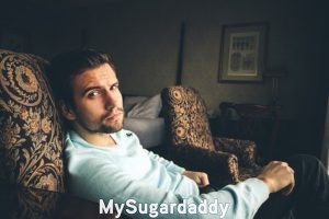 Sugar Daddy maduro: Un hombre sentado sobre un sillón con una expresión seria y profunda. Al lado de el hay otro puesto libre. Parece estar esperando a su pareja, para compartir y vivir una vida exclusiva.
