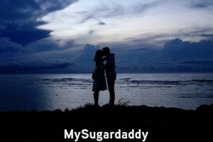 Sugar Daddy maduro: En la imagen vemos a una pareja dándose un beso en un lugar inolvidable. Están a las orillas del mar durante el atardecer. Un escenario muy romántico. 