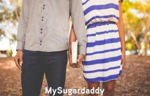 Mentor: Pareja Sugar Mentor: En la imagen vemos a dos personas de pie. Sostiene entre medio de ellos un libro mientras están tomados de la mano. Una pareja que también se concentra en apoyarse mutuamente. Un Sugar Daddy le ayuda a su Sugar Baby a recibir el conocimiento que necesita para ser independiente y encontrar la felicidad.