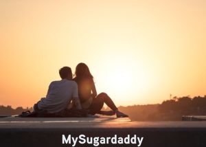 Seducir con Éxito: Dos personas sentadas juntas observando el atardecer sobre un techo de una casa. Él esta sentado detrás de ella buscando su cercanía. Por seguro, ella supo cómo seducir y cautivar su interés. 